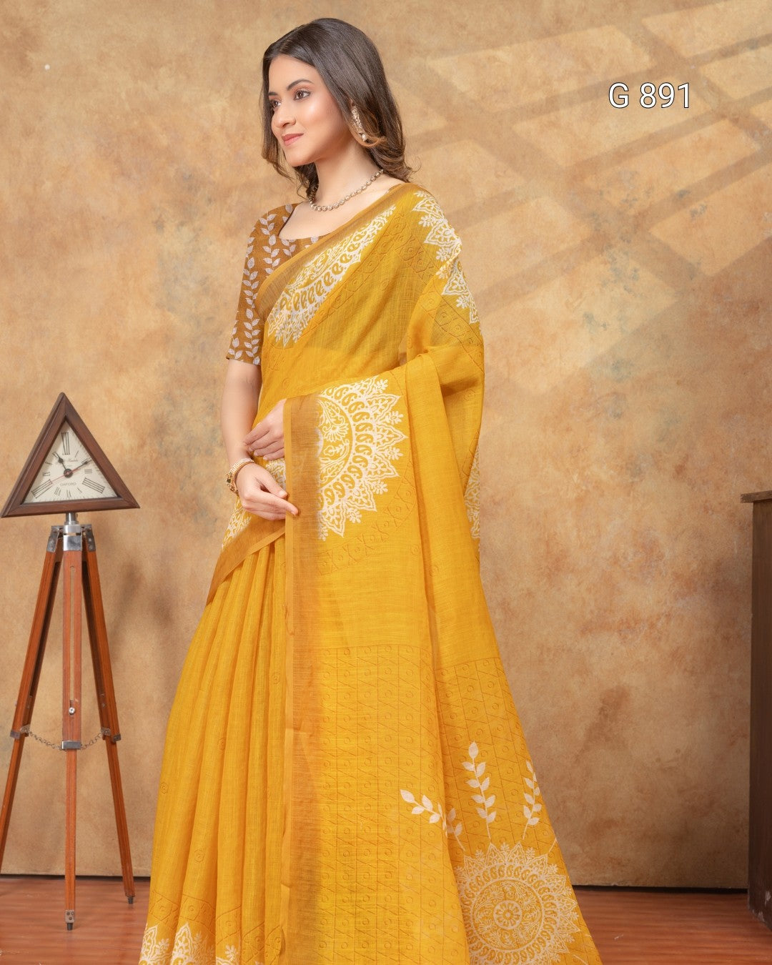 Woman wearing a yellow saree with white patterns against a brown background