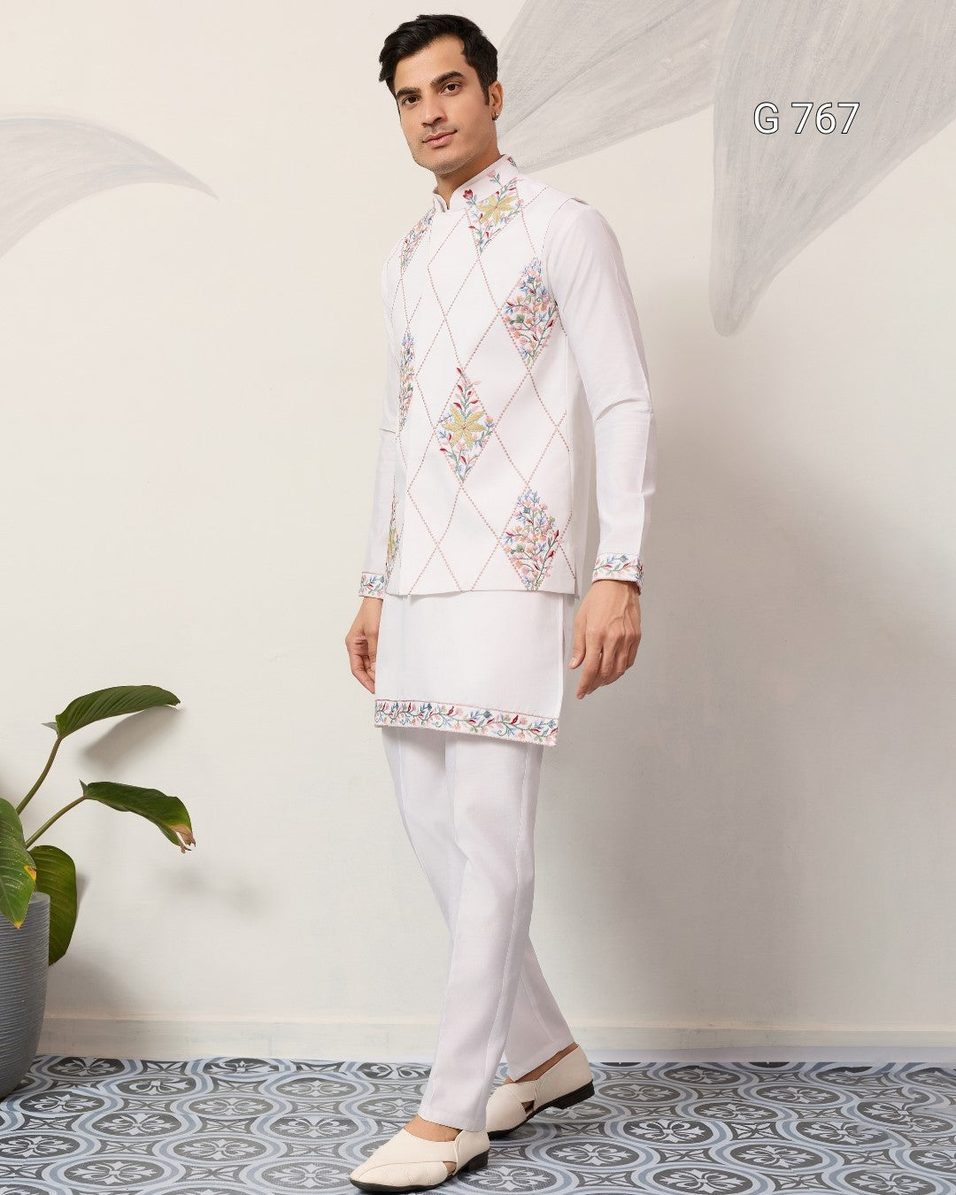 Man wearing a traditional white embroidered kurta with pants in a minimalistic setting.