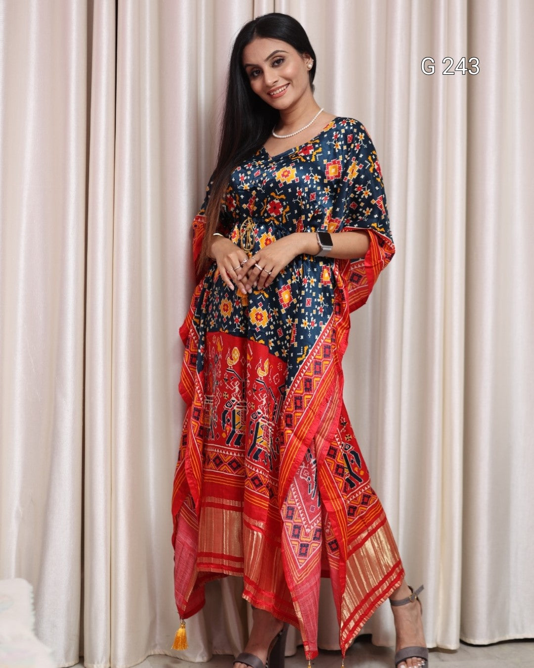 Woman wearing a colorful traditional outfit with a red and blue patterned dress against a white curtain background.