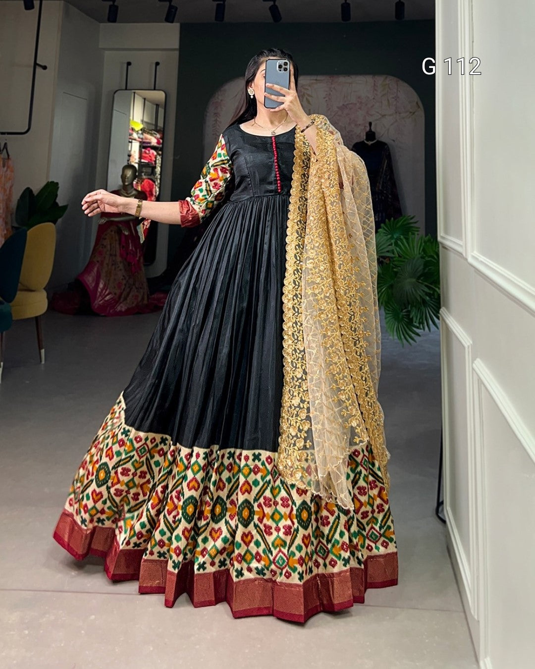 Woman wearing a traditional outfit with a black top and colorful skirt in a room.