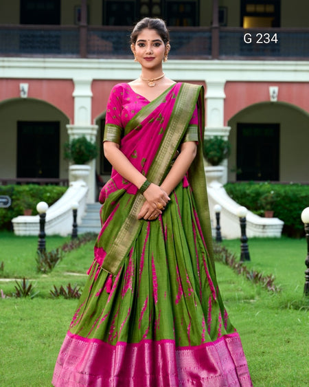 Woman in a green and pink saree standing in a garden with a building in the background
