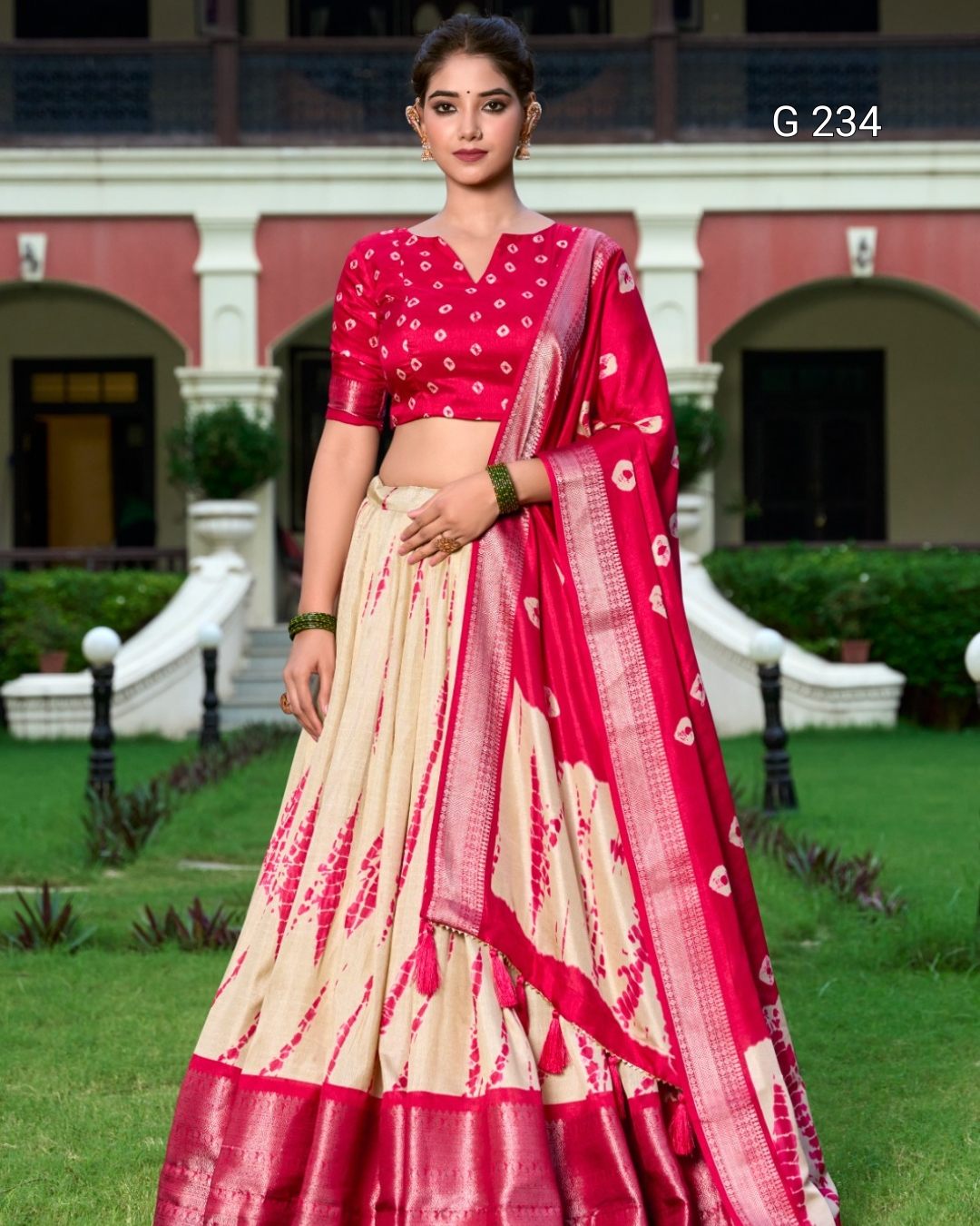 Woman wearing a pink and beige saree with a building and greenery in the background