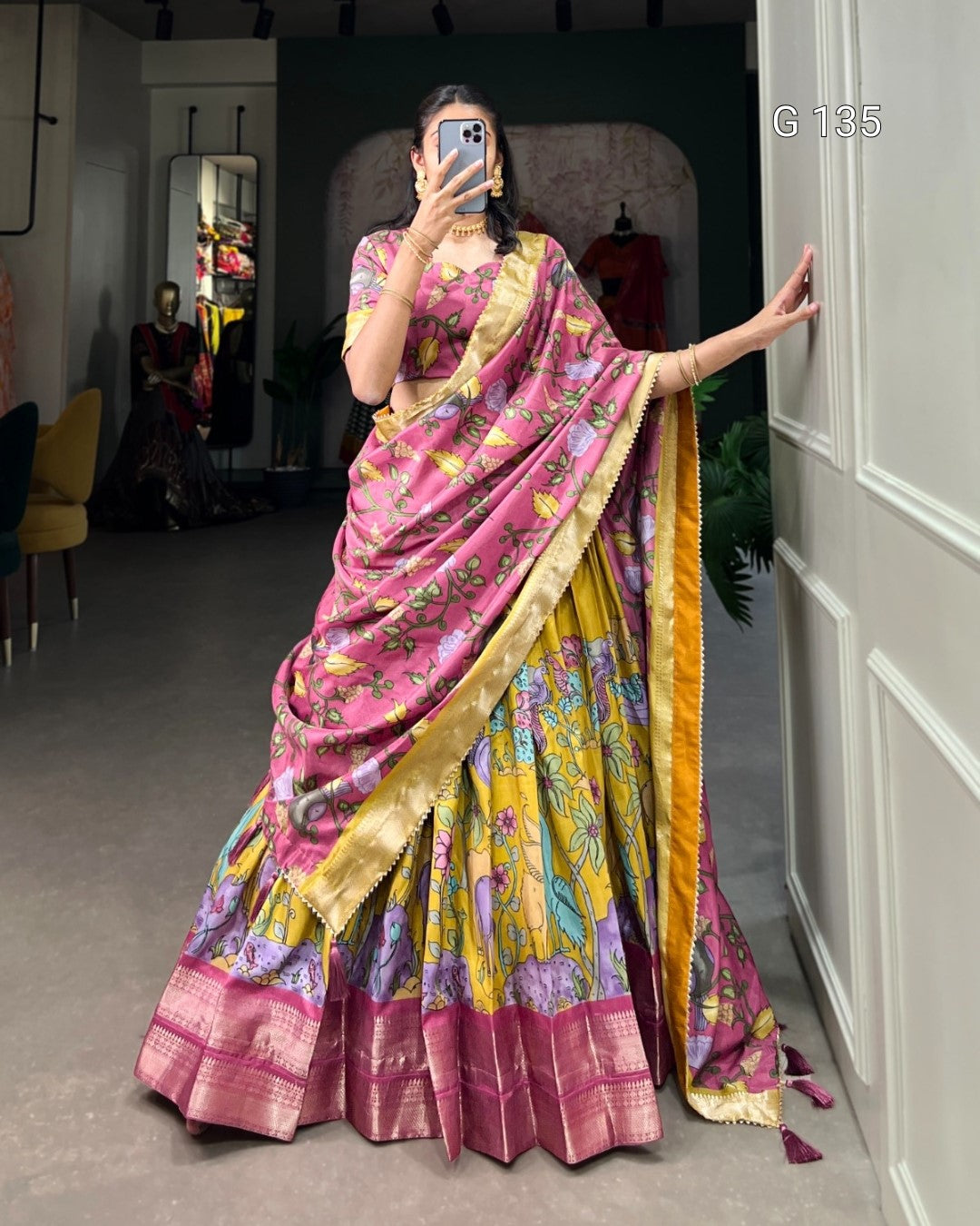 Person wearing a colorful saree taking a mirror selfie in a room.