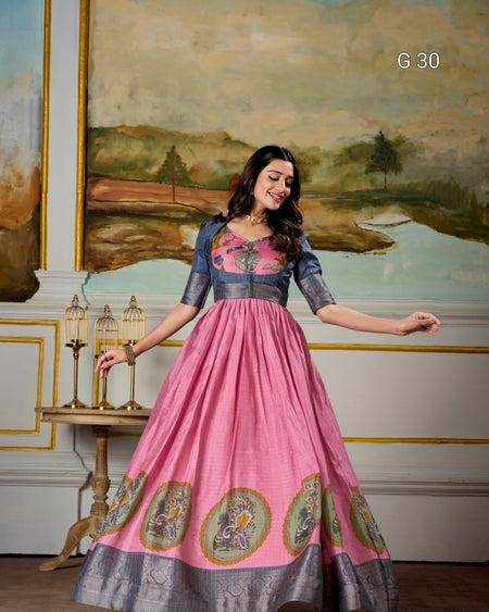 Woman in a pink and gray traditional outfit with intricate designs, standing in a decorated room.