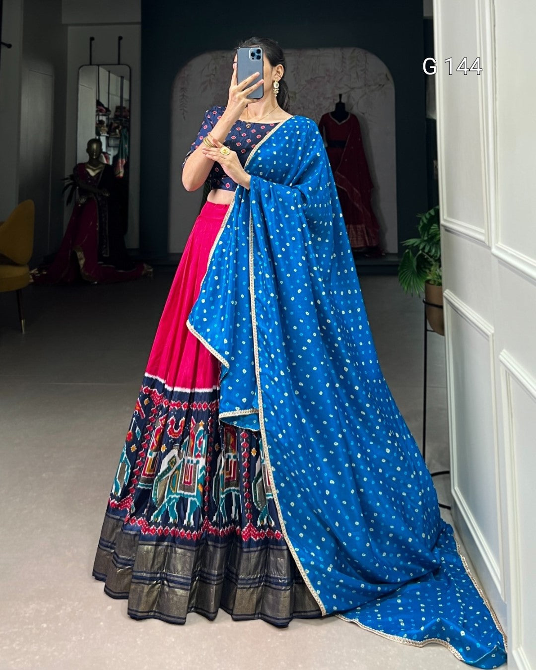 Woman wearing a blue saree with a colorful pattern, standing in a room.