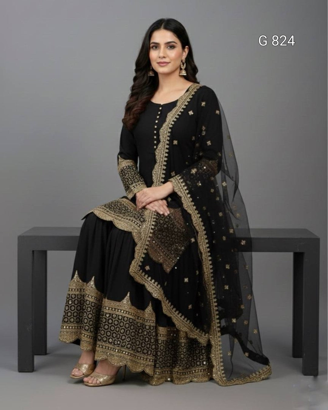 Woman wearing a black and gold traditional outfit sitting on a bench against a gray background.