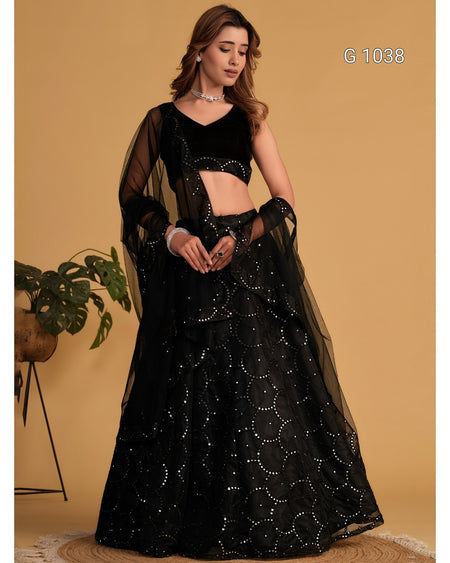 A woman models a black traditional Indian outfit consisting of a velvet crop top, sheer long sleeves, and a heavily embellished flared skirt, set against a solid beige background.
