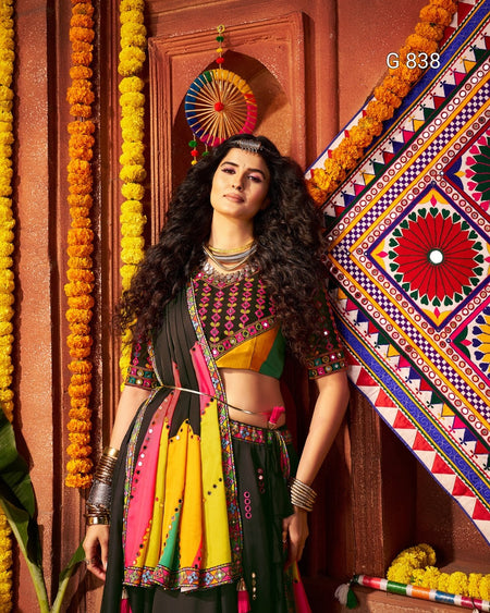 Woman in traditional multicolored outfit standing against a decorated wall with marigold flowers.