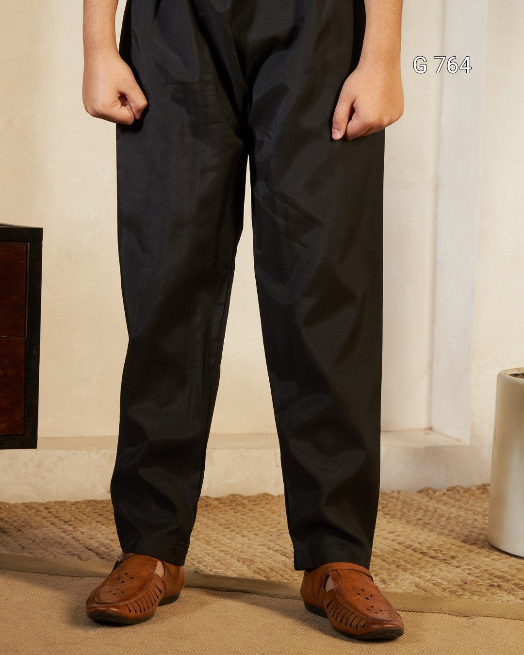 Person wearing black pants and brown shoes standing indoors.
