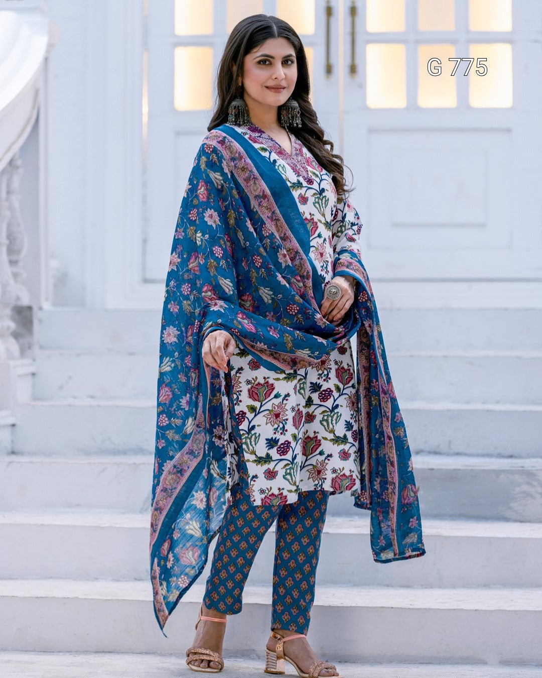 Woman wearing a floral dress with a matching dupatta on a white staircase.
