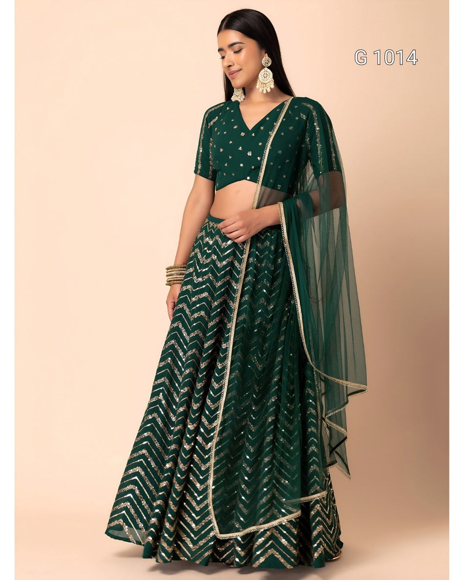A woman modeling a dark green traditional Indian outfit with a V-neck blouse, flared patterned skirt, and sheer dupatta, against a plain beige studio background. The text 'G1014' appears in the top right.