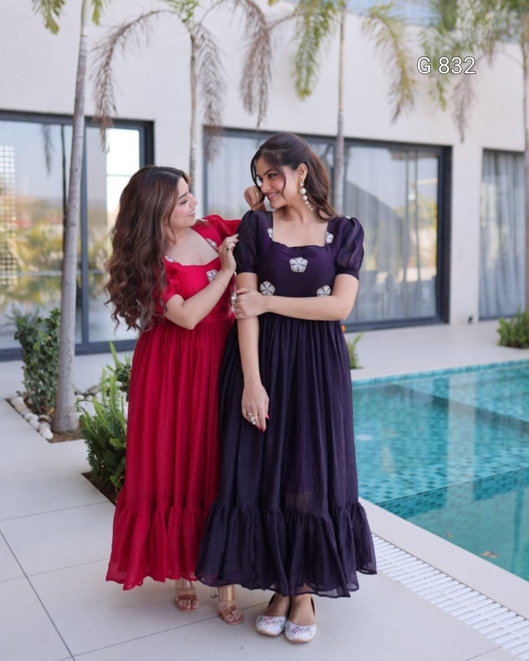 Two women in long dresses standing by a poolside.