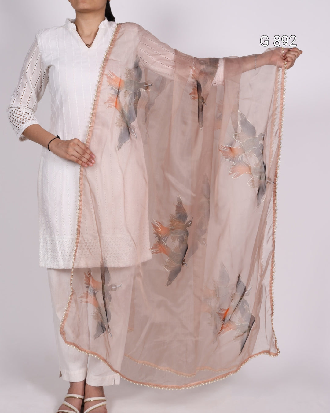 Woman wearing a white kurta with a sheer dupatta featuring bird prints on a plain background