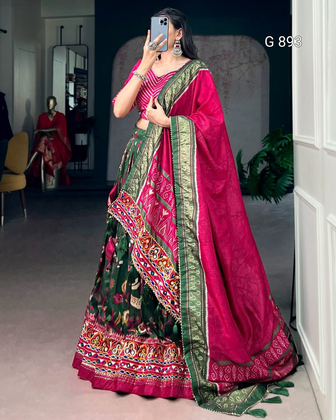 Woman wearing a vibrant pink and green saree with a patterned border, standing indoors.