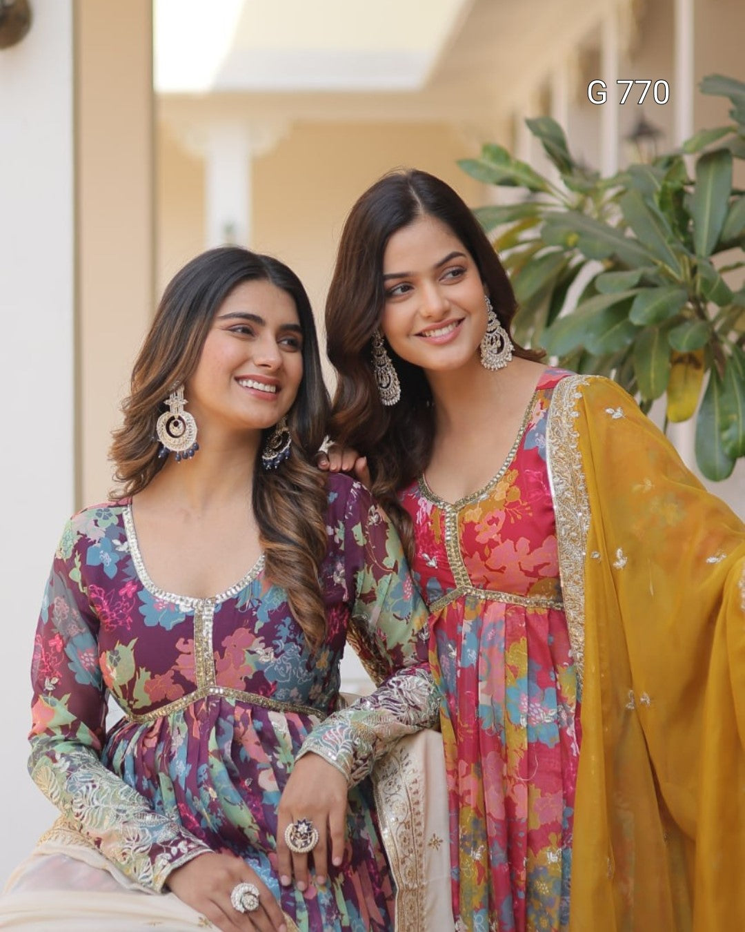 Two women in colorful traditional outfits posing together outdoors.