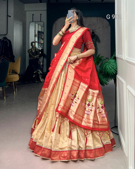 A woman takes a mirror selfie wearing a traditional Indian lehenga choli saree. The saree features a vibrant red body and border with a wide beige/gold zari-embellished skirt and a red blouse with gold embroidery.