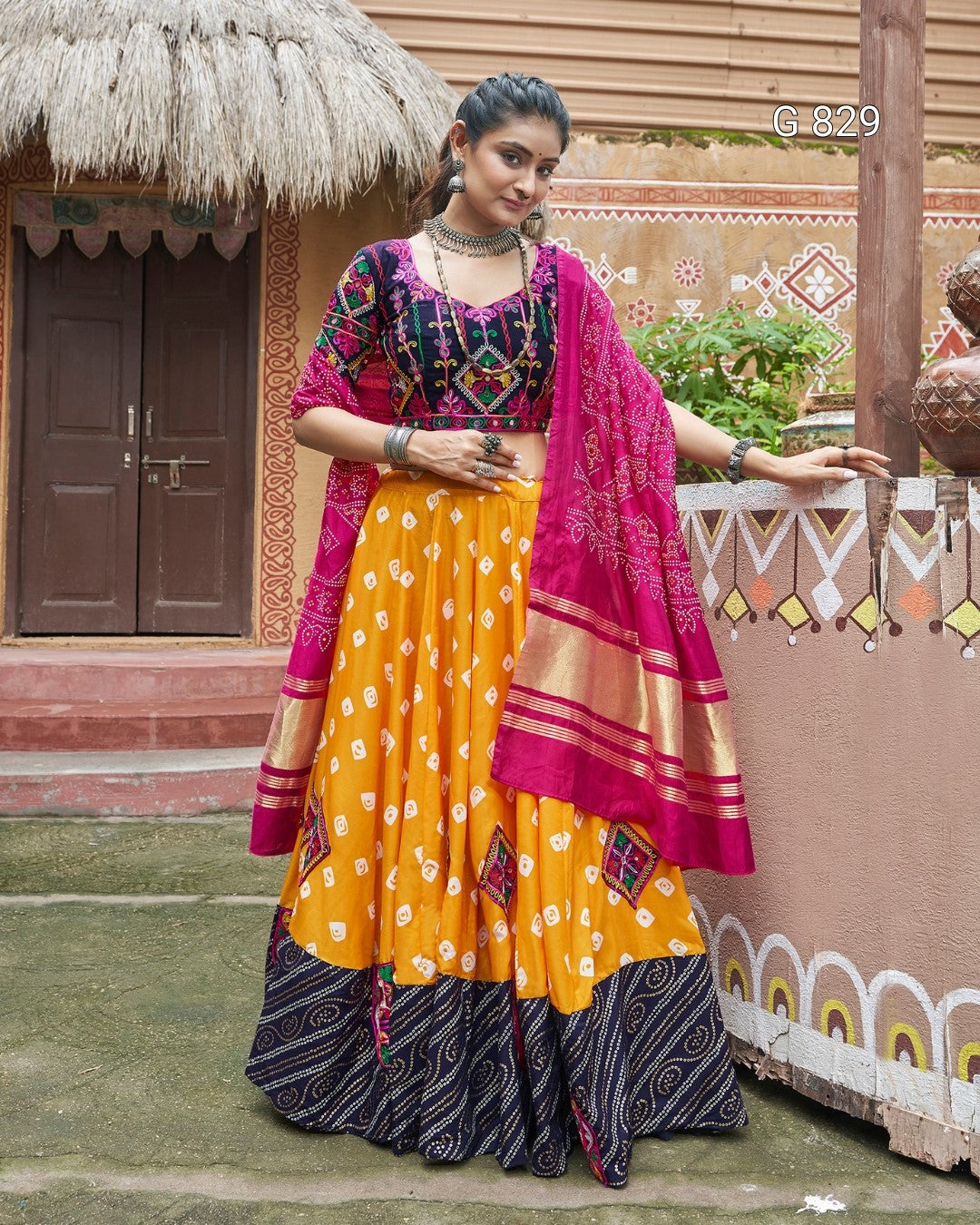 Woman in traditional outfit with yellow and pink elements standing in front of a decorative wall.
