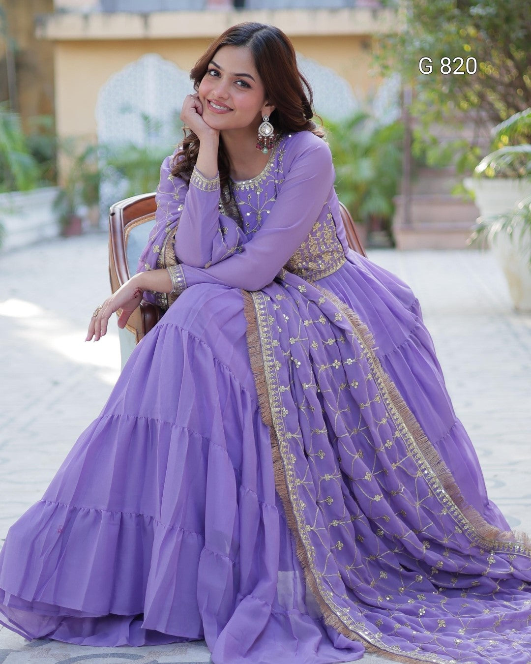Woman in a purple traditional outfit with gold embroidery sitting outdoors.