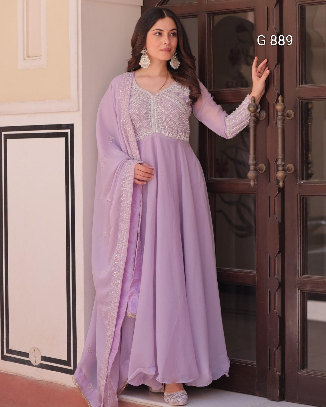 Woman in a lavender traditional outfit standing in front of a wooden door.