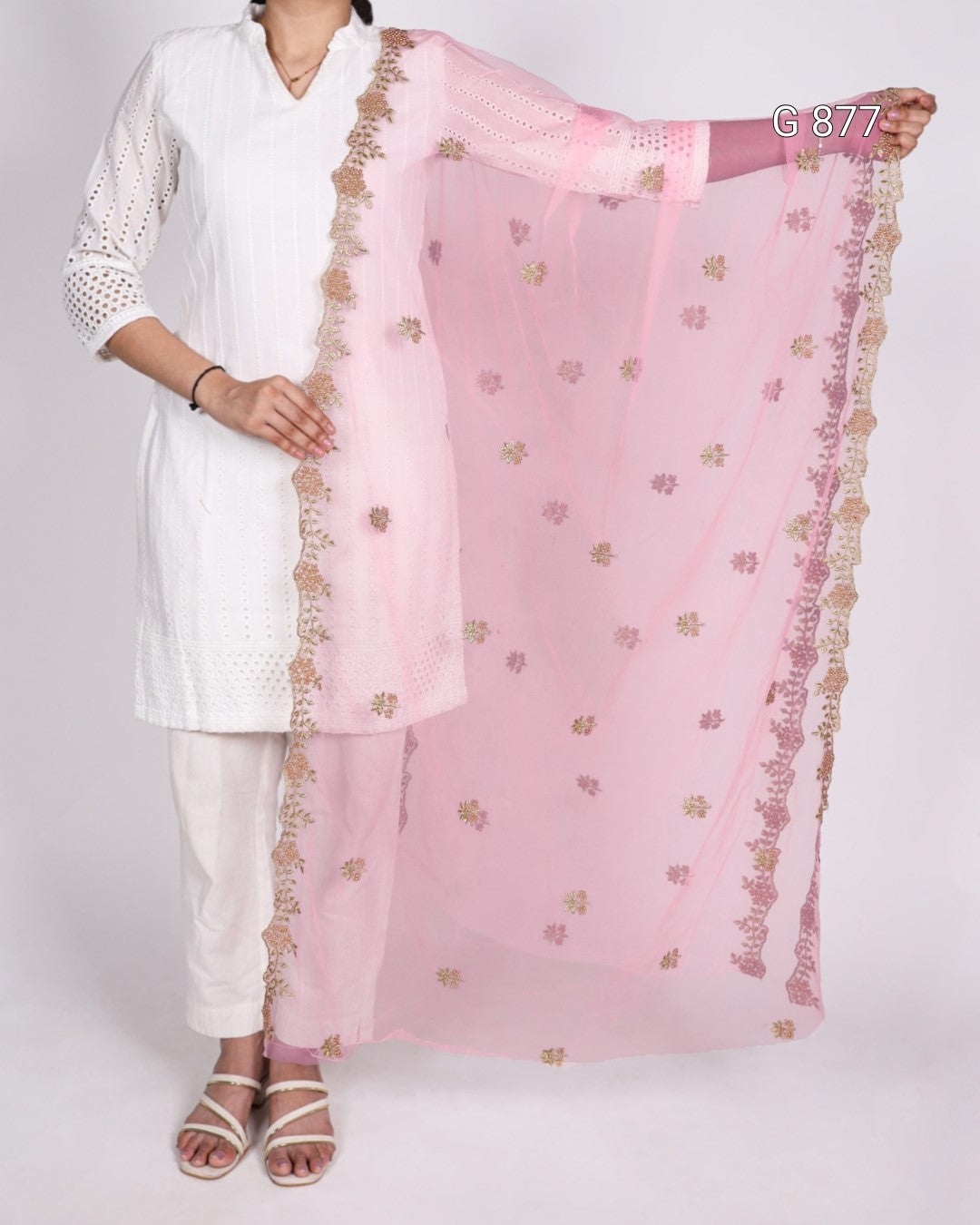 Person wearing a white outfit with a pink dupatta featuring gold patterns on a plain background