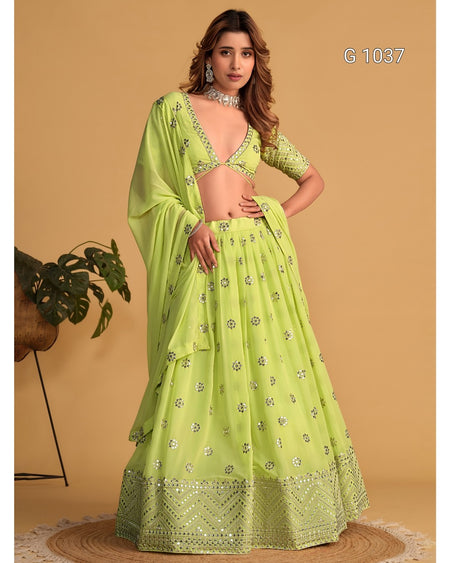 A woman models a bright lime green traditional Indian lehenga choli set with silver mirror work embroidery, set against a warm beige background.