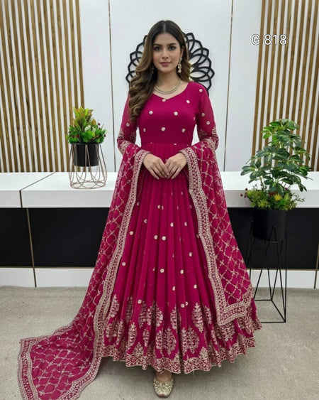 Woman in a pink traditional outfit with intricate designs standing indoors.