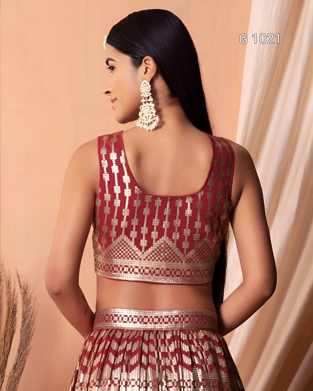 A woman shown from the back wearing a sleeveless maroon and gold patterned traditional top with a matching skirt, against a warm beige backdrop with draped fabric.