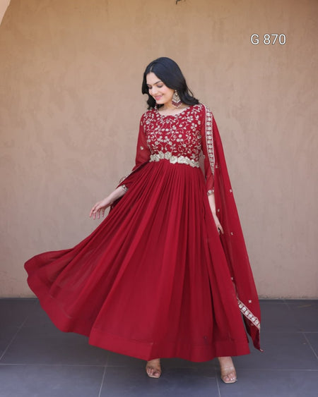 Woman wearing a red traditional outfit with gold details against a beige wall.