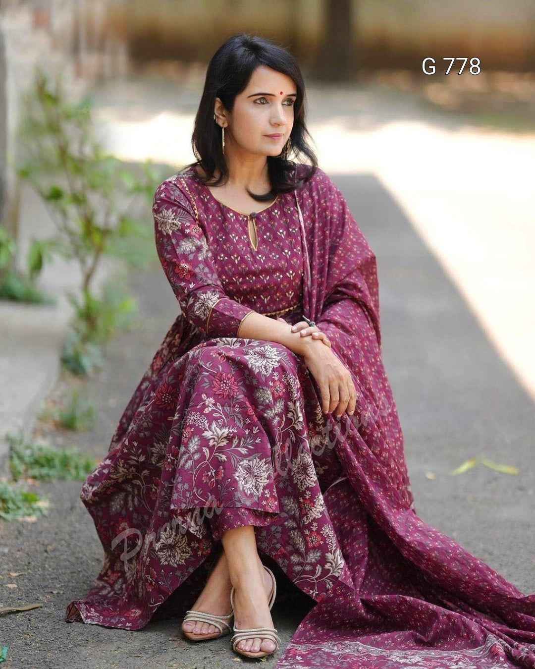 Woman in a long, patterned dress sitting outdoors on a path.