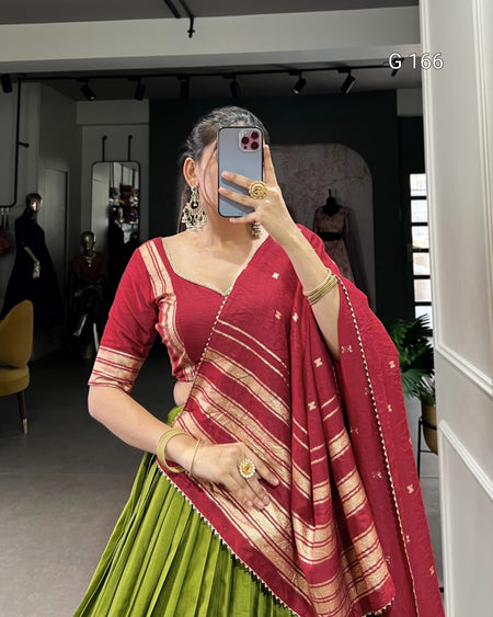 Person wearing a red and green saree with gold jewelry indoors.