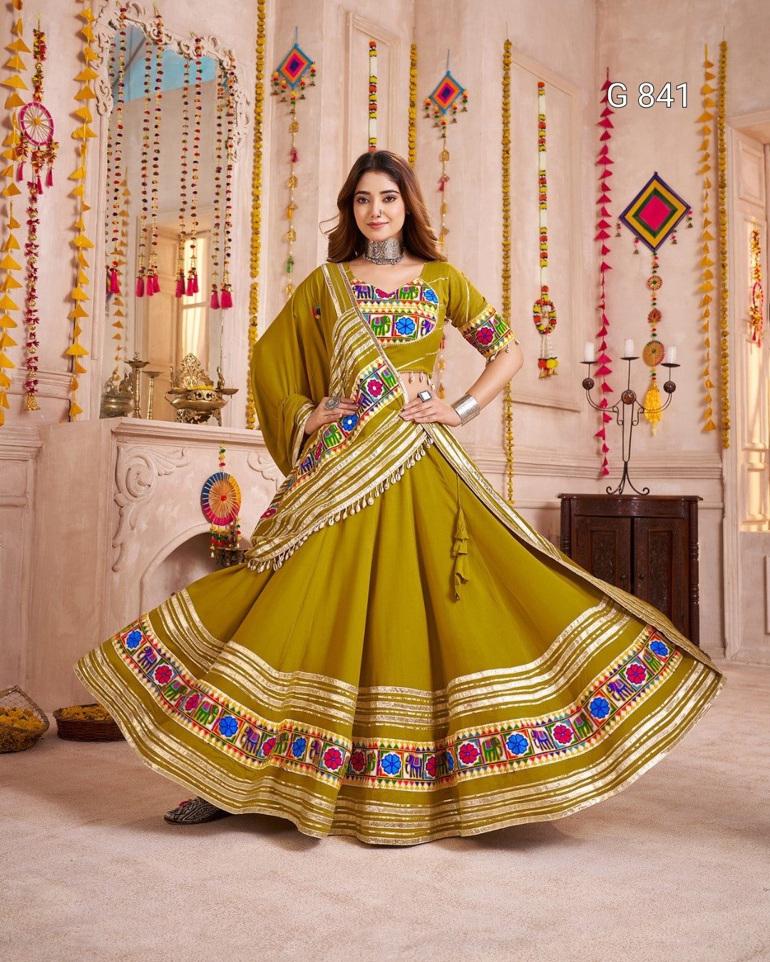 Woman in a green traditional outfit with colorful patterns in a decorated room.