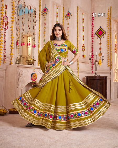 Woman in a green traditional outfit with colorful patterns in a decorated room.