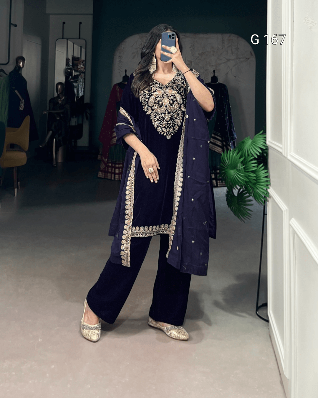 Person wearing a navy blue traditional outfit with intricate silver embroidery in a room.