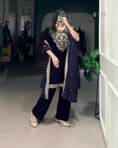 Person wearing a navy blue traditional outfit with intricate silver embroidery in a room.