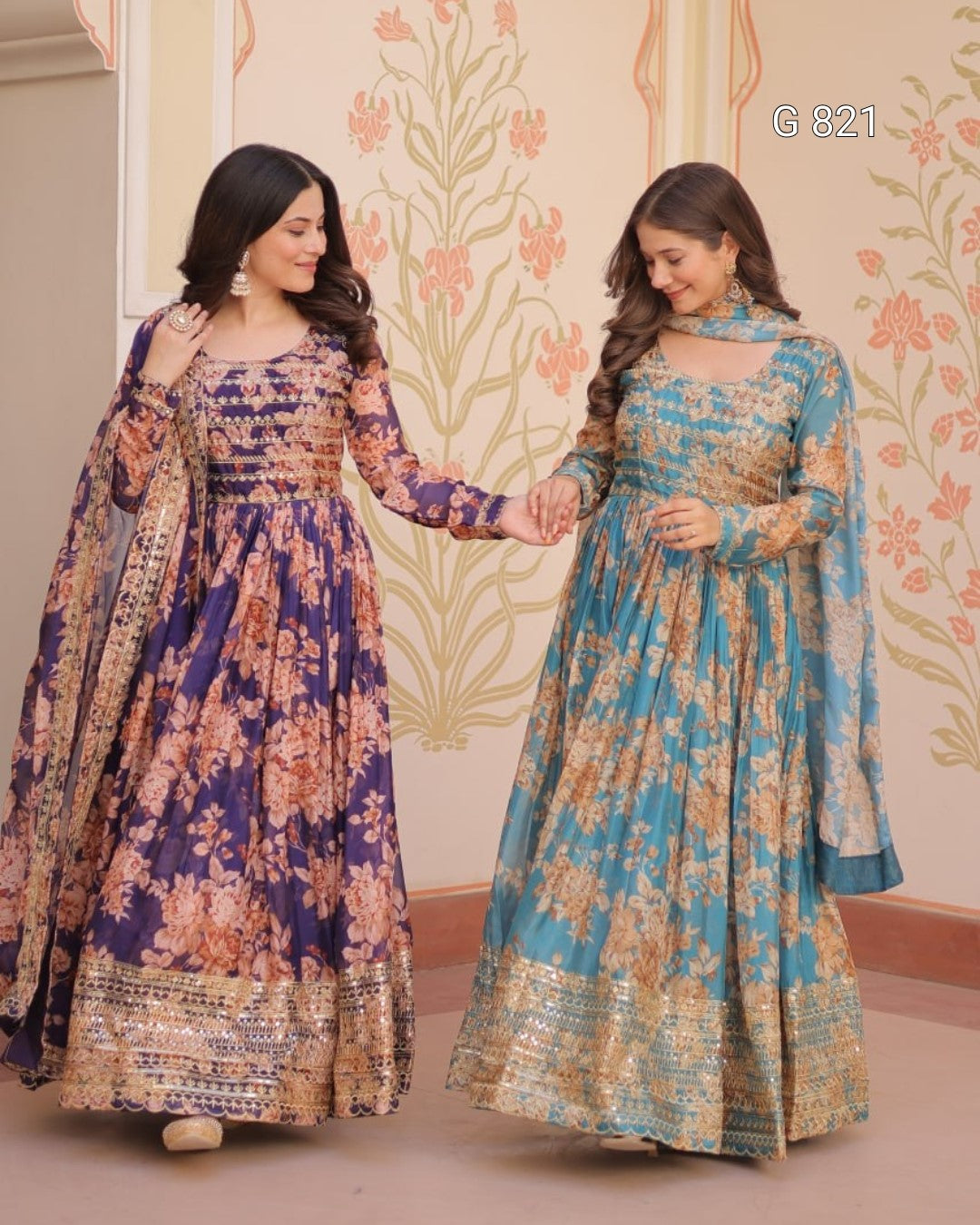 Two women in floral dresses standing against a decorative wall.