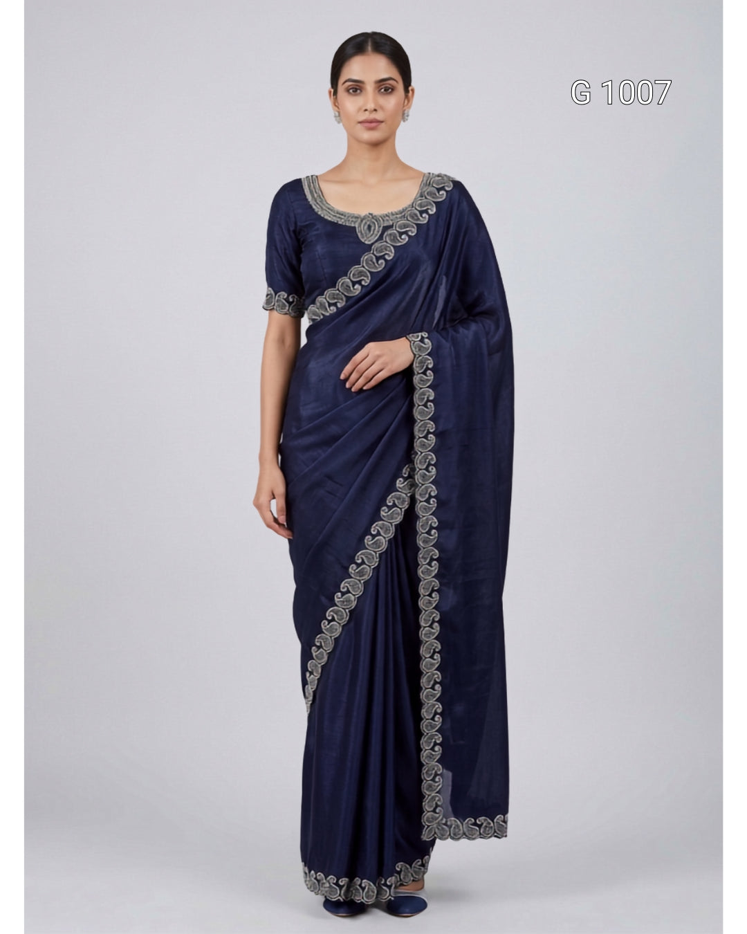 A woman modeling a navy blue saree with silver floral embroidery along the border and sleeve, standing against a light gray studio background. The number 'G 1007' appears in the top right corner.