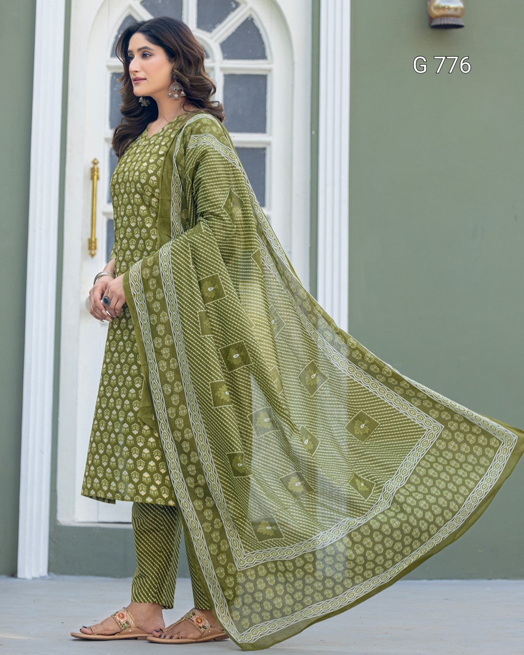 Woman wearing a green traditional outfit with a matching dupatta in front of a white door.