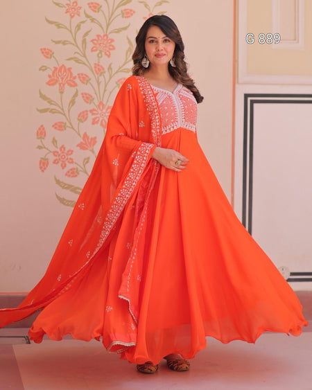 Woman wearing an orange traditional outfit with white embroidery in a decorated room.