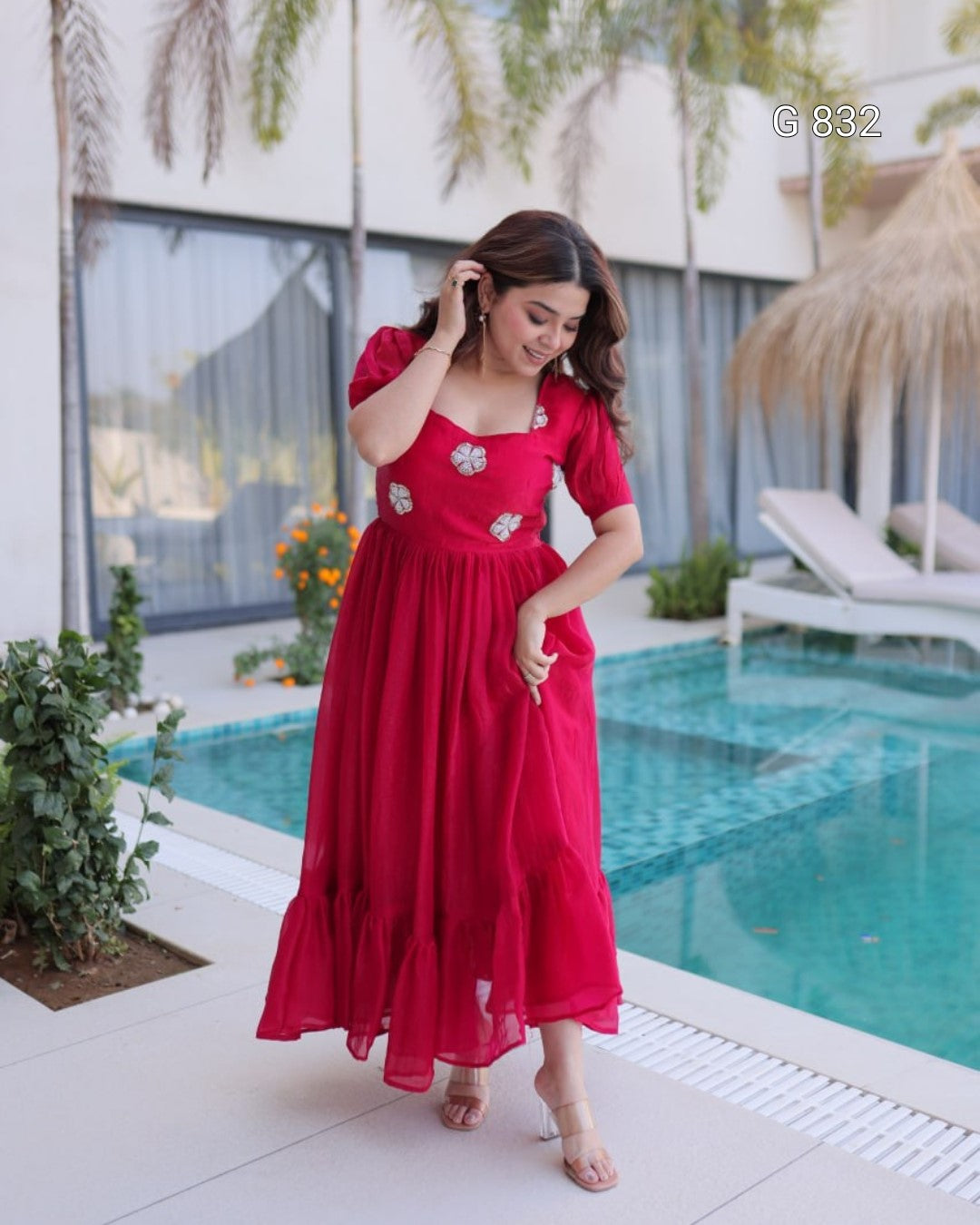 Woman in a red dress standing by a pool with greenery around