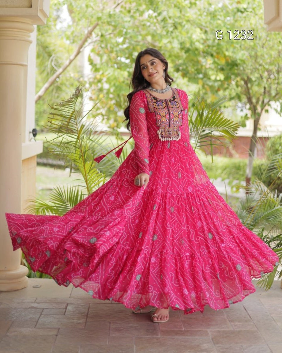 A woman wearing a bright pink embroidered Anarkali gown with a flared skirt, standing on a tiled patio in front of a garden and columns. The number 'G1232' is visible in the top right corner.
