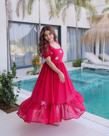 Woman in a pink dress standing by a pool with a building and plants in the background