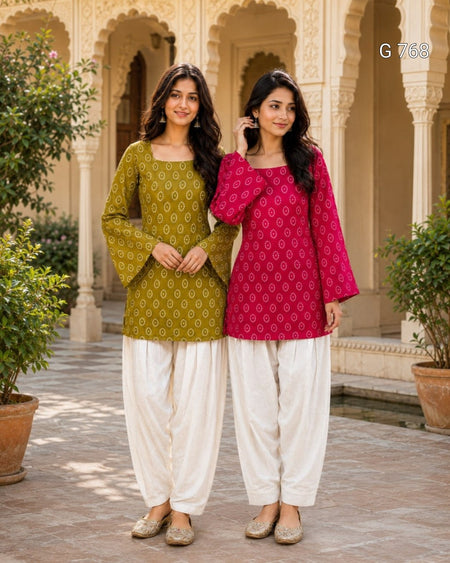 Two women in traditional green and pink kurta with white pants standing in a decorative outdoor setting.