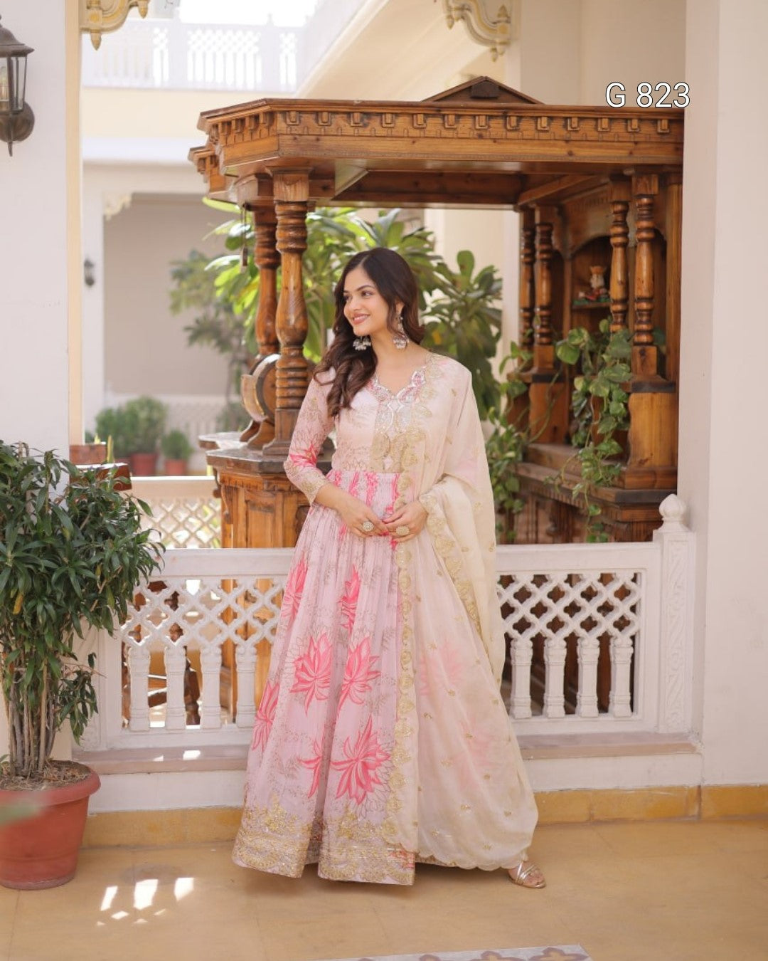 Woman in a traditional outfit standing in a decorated indoor setting with plants and wooden architecture.