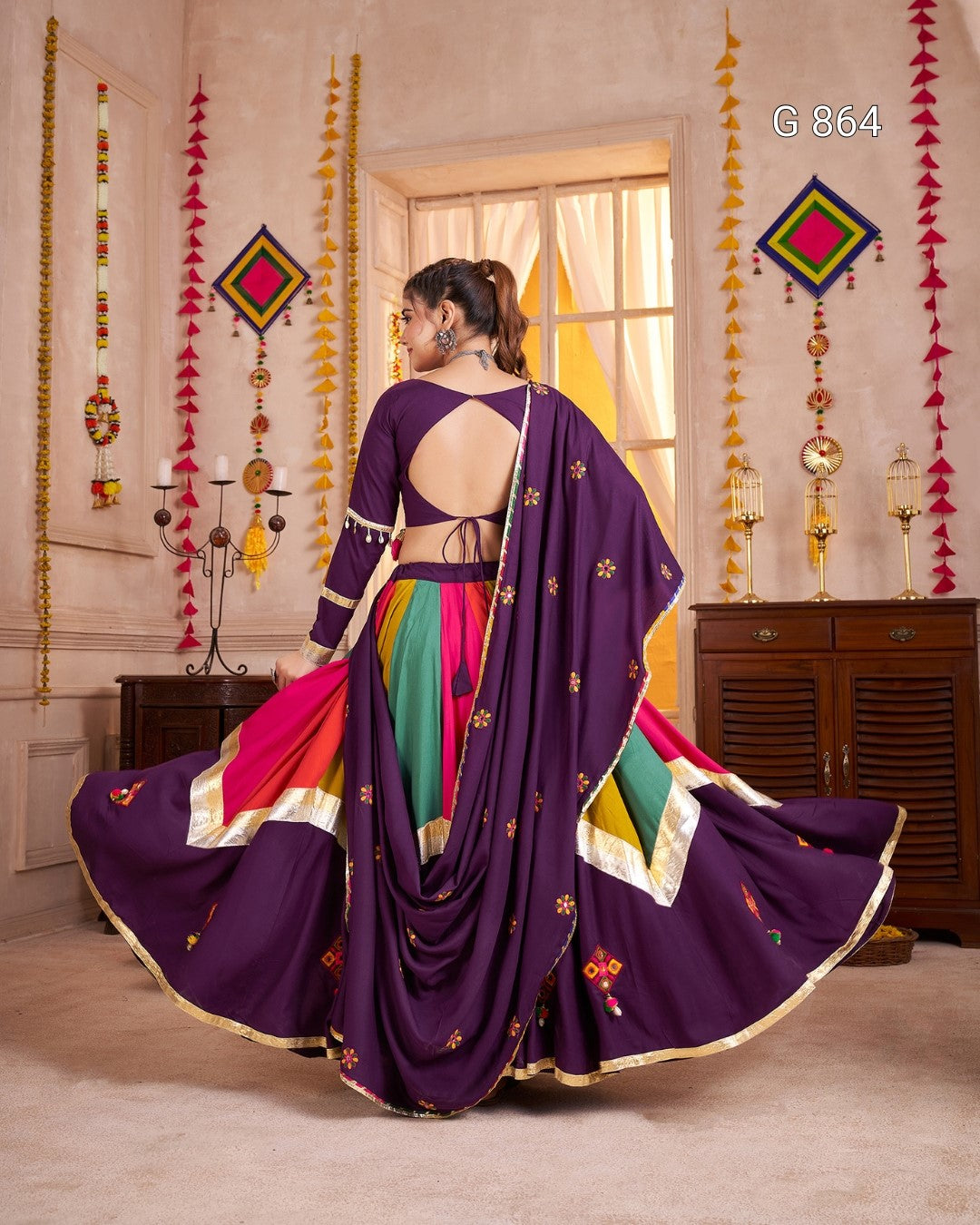 Woman wearing a colorful saree with a purple blouse in a decorated room.