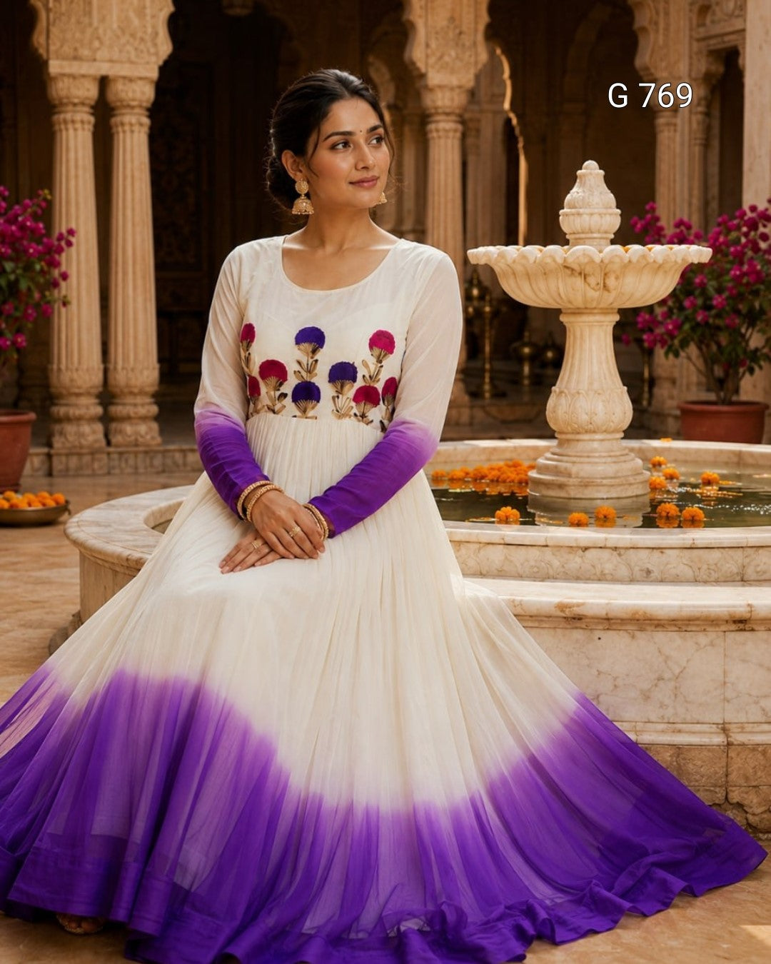 Woman in a white and purple dress with floral patterns sitting by a fountain.