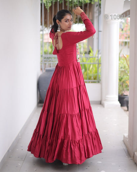 A woman modeling a long-sleeved, tiered red maxi dress in a covered walkway with white pillars and green plants in the background.