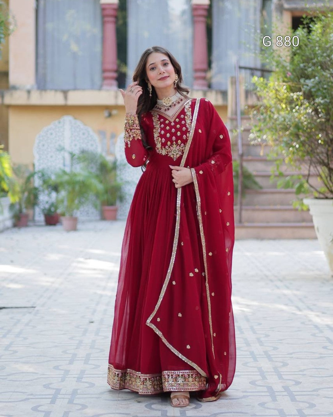 Woman in a red traditional outfit with gold embroidery standing outdoors.