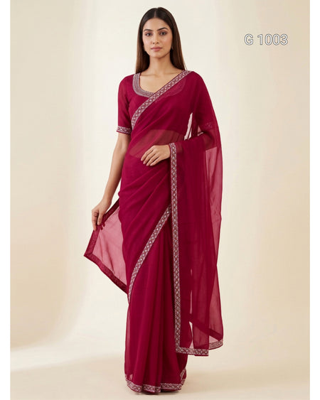 A woman modeling a deep magenta saree with silver patterned borders, standing against a plain beige studio background. The text 'G 1003' is visible in the top right corner.