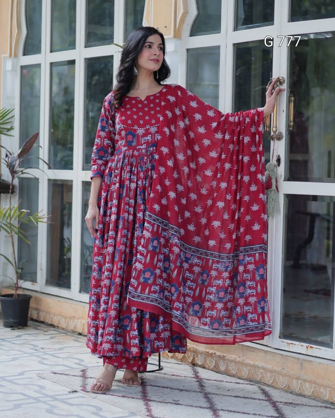 Woman wearing a red and blue patterned dress standing in front of a glass door.