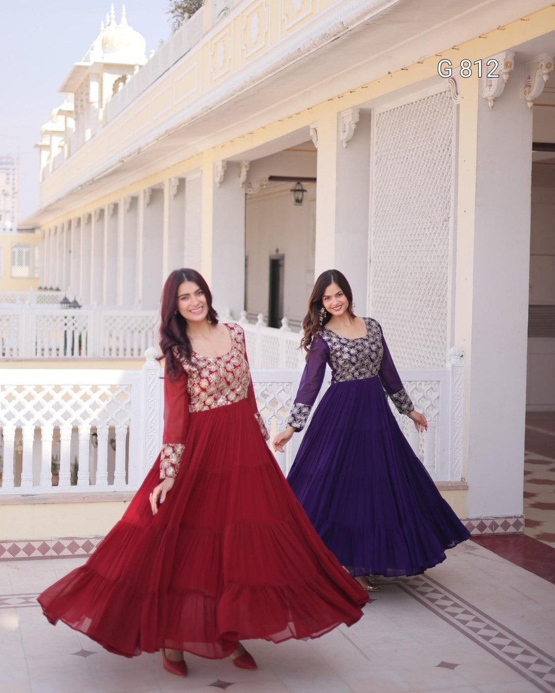 Two women in red and purple dresses standing in front of a white architectural structure.